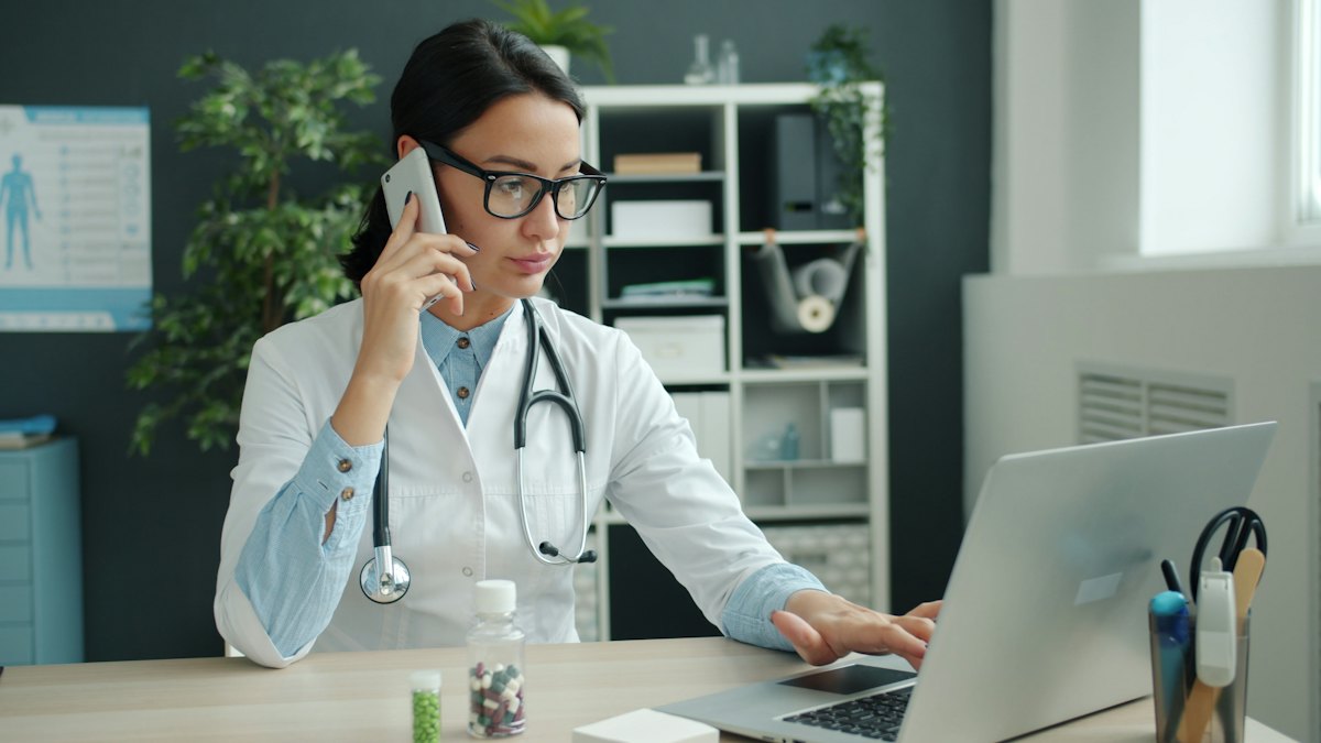 A doctor on the phone while working on a laptop in her office